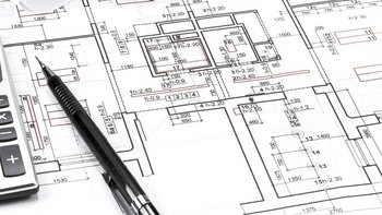 Ein detaillierter Bauplan mit Maßangaben, einem Taschenrechner und einem Stift, die auf einem Tisch liegen.